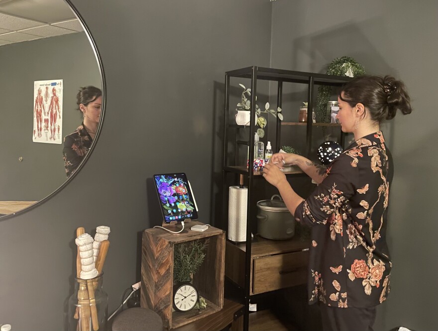 Noah Afshar in front of a shelf in their studio. Afshar is wearing a black shirt with a flower print. 